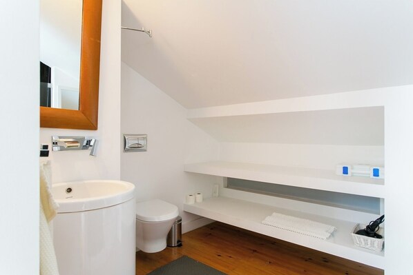 A modern bathroom with a white sink, toilet, and shower. There are shelves with toiletries and a mirror above the sink. - Bairro Alto perfect daylight DUPLEX!! Great WI-FI! (Lisboa)