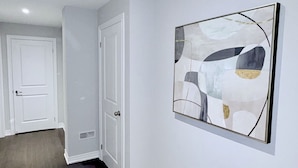 Un couloir doté d’un plancher en bois foncé, de murs blancs et d’un grand tableau abstrait.
