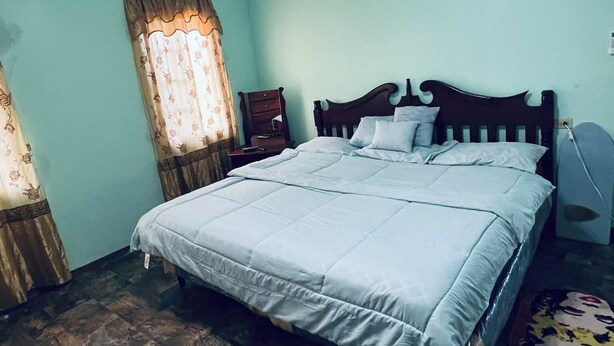 Une chambre à coucher avec un lit, un ventilateur de plafond, une table de chevet et une fenêtre avec des rideaux.