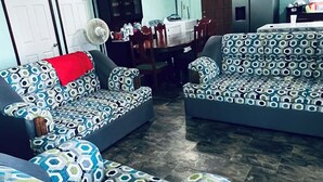 Un salon avec des canapés à motifs, une table à manger, des ventilateurs de plafond et un réfrigérateur.