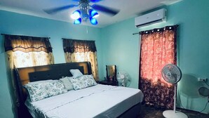 Une chambre à coucher avec un lit, un ventilateur de plafond, un climatiseur et un ventilateur sur pied.