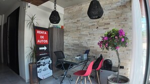 Un interior moderno con una mesa de vidrio, sillas rojas, una pared de ladrillo y un cartel de alquiler de coches.