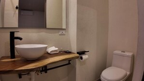 Un baño con lavabo blanco, grifo negro, encimera de madera, inodoro y espejo sobre el lavabo.