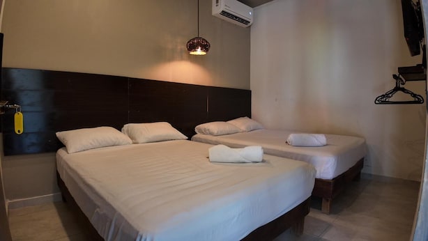 Habitación de hotel con dos camas, una lámpara colgante, un equipo de aire acondicionado y un perchero de pared.