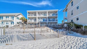 Un hôtel situé en bord de mer, doté de nombreux balcons, avec une plage de sable devant et un ciel bleu dégagé.