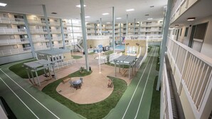Un vestíbulo de hotel de varios niveles con balcones, zona de piscina y mobiliario exterior.