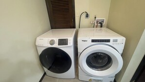 Deux machines à laver à chargement frontal, une Samsung et une Whirlpool, dans une buanderie dont le sol est carrelé et qui est dotée d’une porte avec un volet marron.