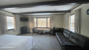 Una habitació d'hotel amb un llit, un sofà de pell, una taula de treball amb una cadira i una televisió.