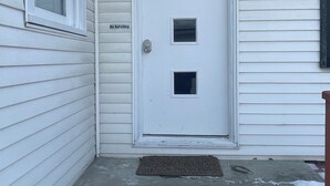 Une maison blanche avec une porte d’entrée, une petite fenêtre et un paillasson.