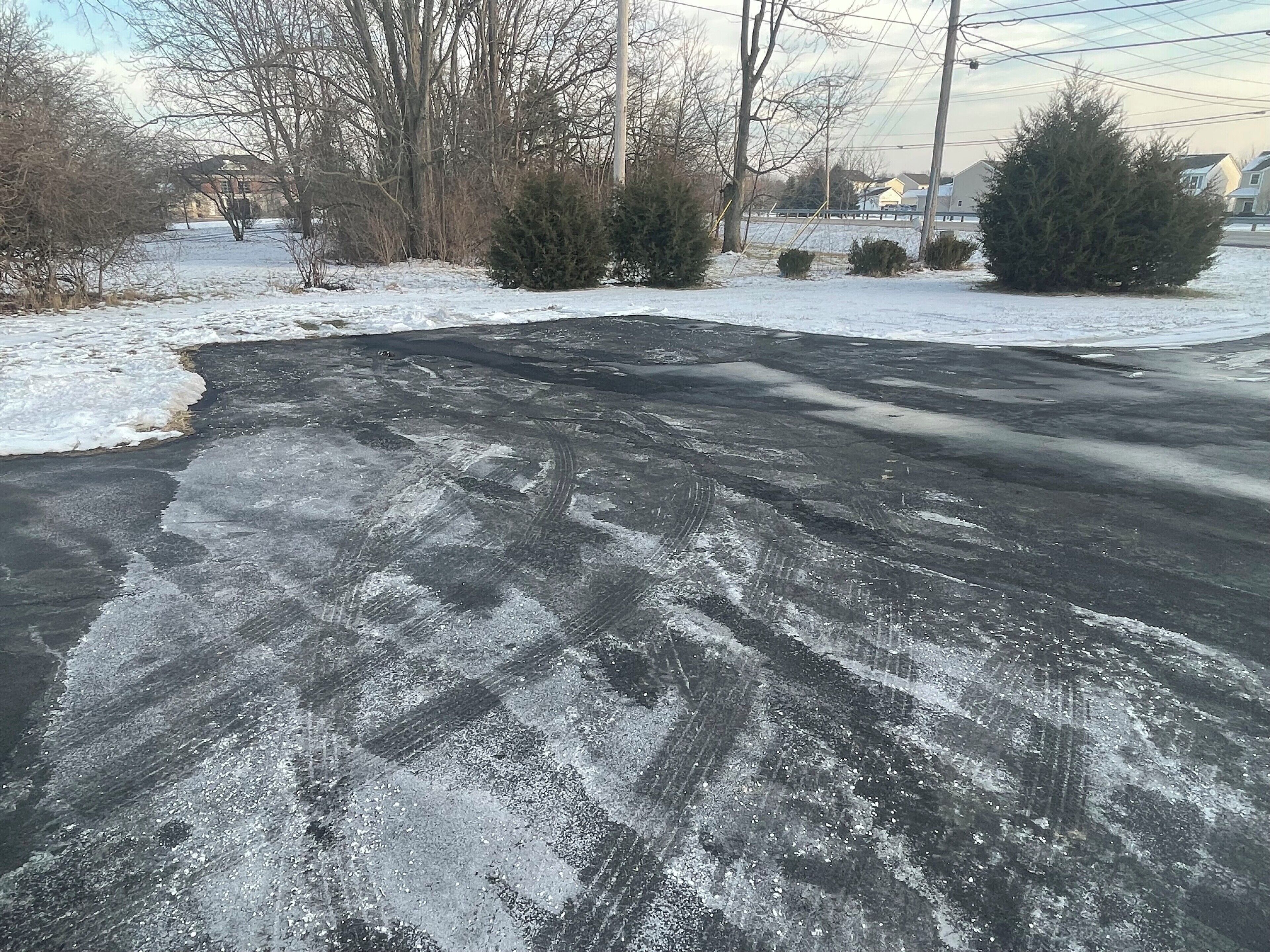 A snow-covered road with visible tire tracks and patches of snow.