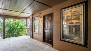 A covered porch with a concrete floor, a dark wooden door, and a window with blinds. - Modern 1 Bed - Gated - Reserved Parking (Oklahoma City)