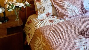 A wooden-paneled room with a bed, floral bedding, and a vase with flowers on a nightstand. - Cabin anny 1 (Vara Gruesa)