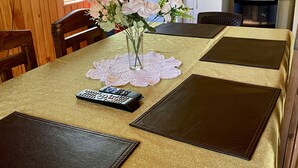 A dining table with a lace doily, a vase with flowers, and remote controls. - Cabin anny 1 (Vara Gruesa)
