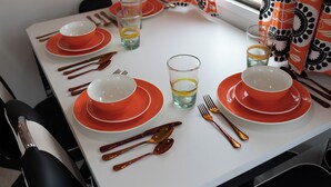 A dining table set with red and white plates, bowls, and cutlery. - 1952 Royal Spartanette Trailer @ Teepee Drive-In (Sapulpa)