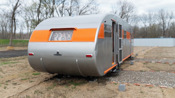 A stationary train car with a rear door, parked on a gravel surface with trees in the background. - 1952 Royal Spartanette Trailer @ Teepee Drive-In (Sapulpa)