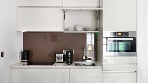 Et moderne køkken med hvide skabe, kaffemaskine, elkedel og indbygget ovn.