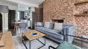 Ein modernes Wohnzimmer mit Backsteinwand, einer Couch, einem Couchtisch und einer Küche im Hintergrund.
