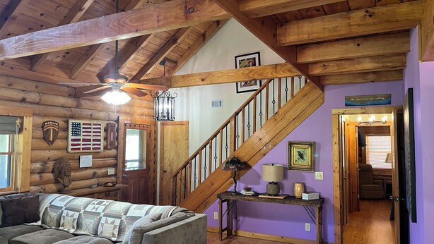 A log cabin interior with a wooden staircase, a sofa, a table, and a wall with framed pictures. - Lavender Gap Farm. True Log cabin on 12 acre flower farm. Near AT / Nat Forest (Suches)