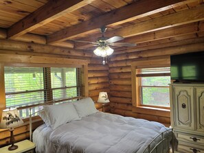 Une chambre dans un chalet en rondins, avec un lit, un ventilateur de plafond, une commode et un téléviseur.