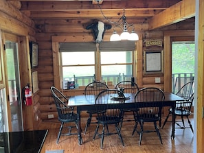 L’intérieur d’un chalet en bois comprend une table à manger, des chaises, un lustre, un extincteur et une fenêtre donnant sur un paysage verdoyant.