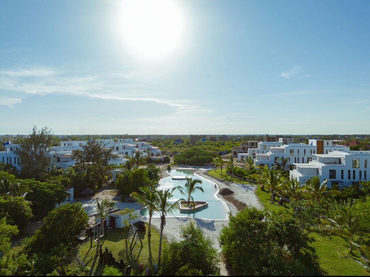 Un resort con diversi edifici bianchi, una piscina centrale e vegetazione circostante.