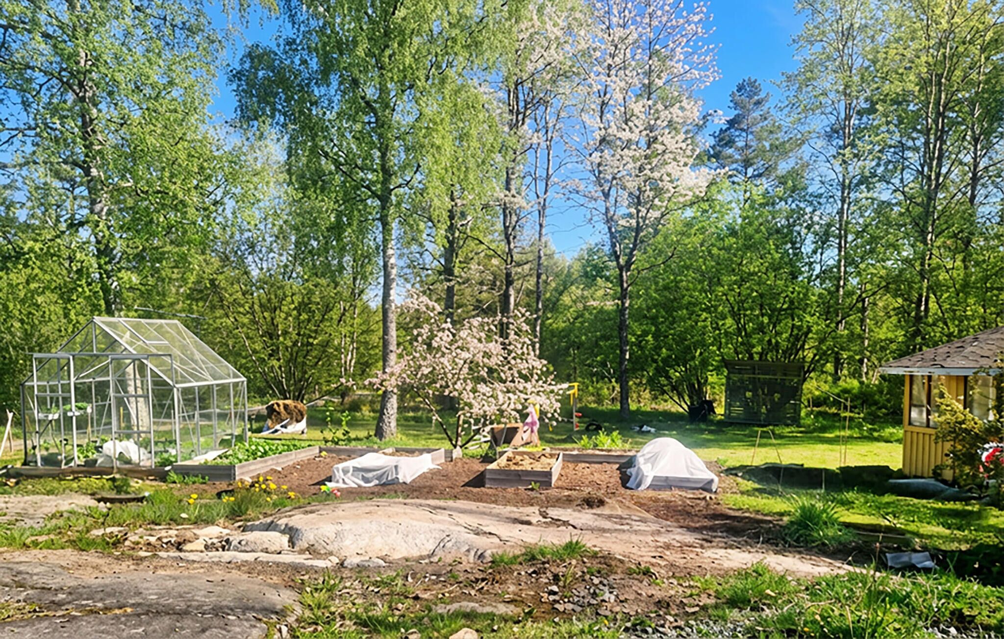 Uma estufa, uma área coberta e um pequeno galpão em um jardim.