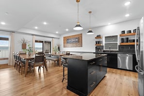 A modern kitchen with a central island, black cabinetry, stainless steel appliances, and a dining area with wooden furniture. - Large Lakeview Lodge with Pool Table & Hot Tub (Hollister)