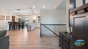 A spacious living area with a dining table, kitchen in the background, and a staircase leading to upper floors.