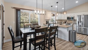 A modern kitchen with white cabinets, stainless steel appliances, and a dining area with a wooden table and chairs.