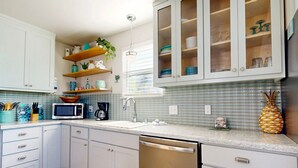 A kitchen with white cabinets, a microwave, a sink, and a dish rack. - Pet Friendly, Golf Cart Accessible, Old Town Port A (Port Aransas)