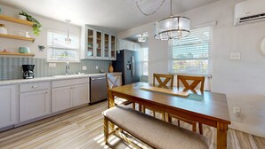 A modern kitchen with white cabinets, a wooden dining table, and a bench. - Pet Friendly, Golf Cart Accessible, Old Town Port A (Port Aransas)