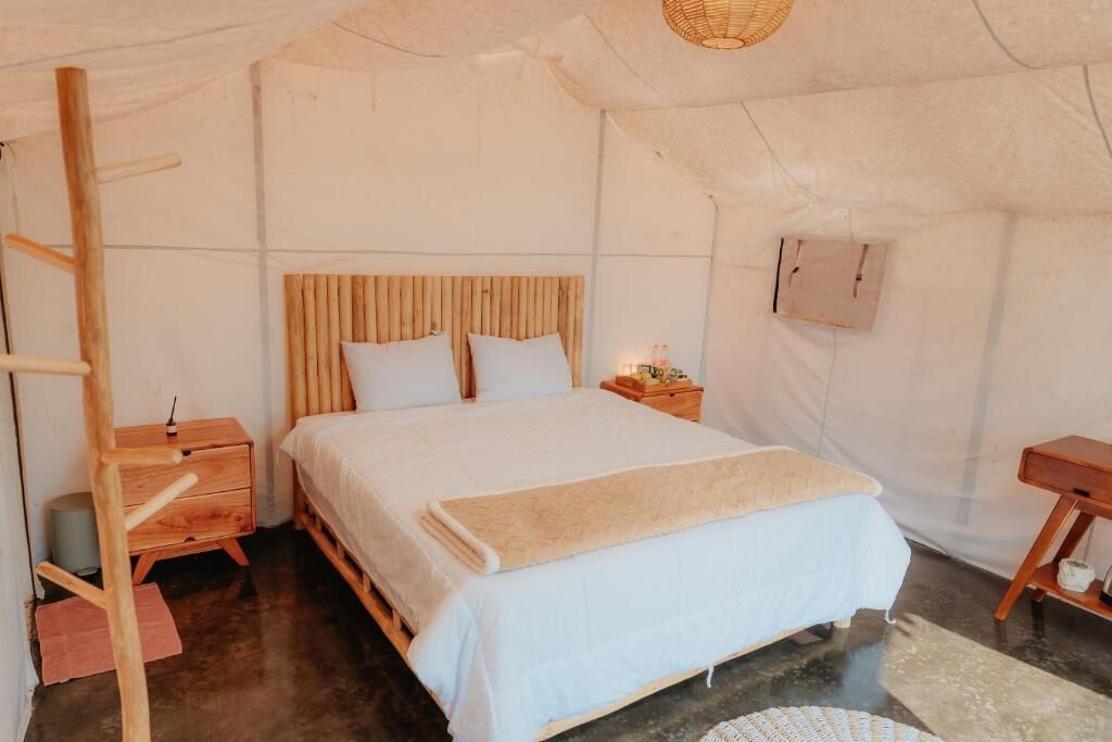 A cozy, well-lit tent-style bedroom with a wooden bed, a nightstand, and a small wooden table.
