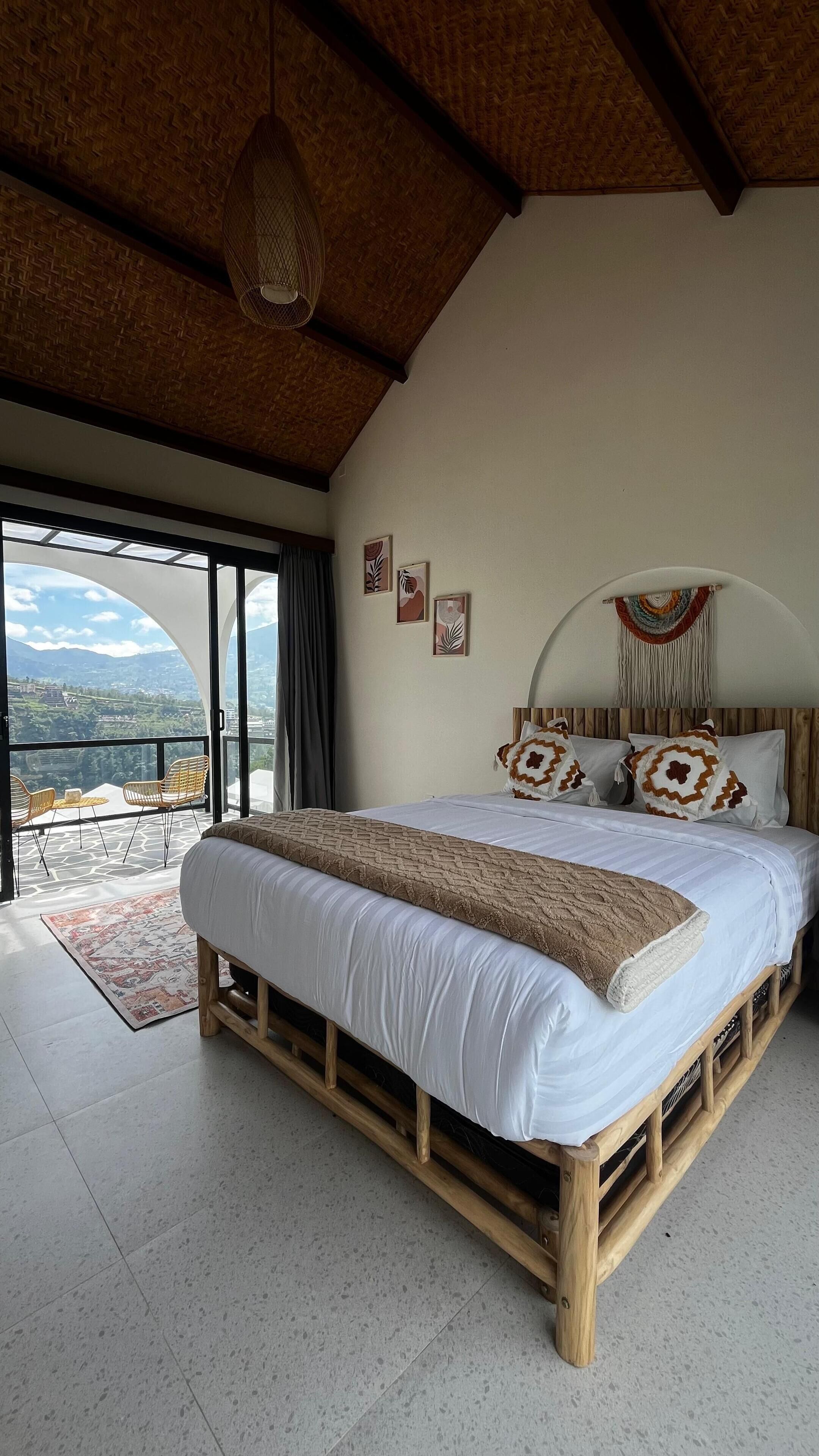 A bedroom with a large bed, a view of the outdoors, and a ceiling fan.