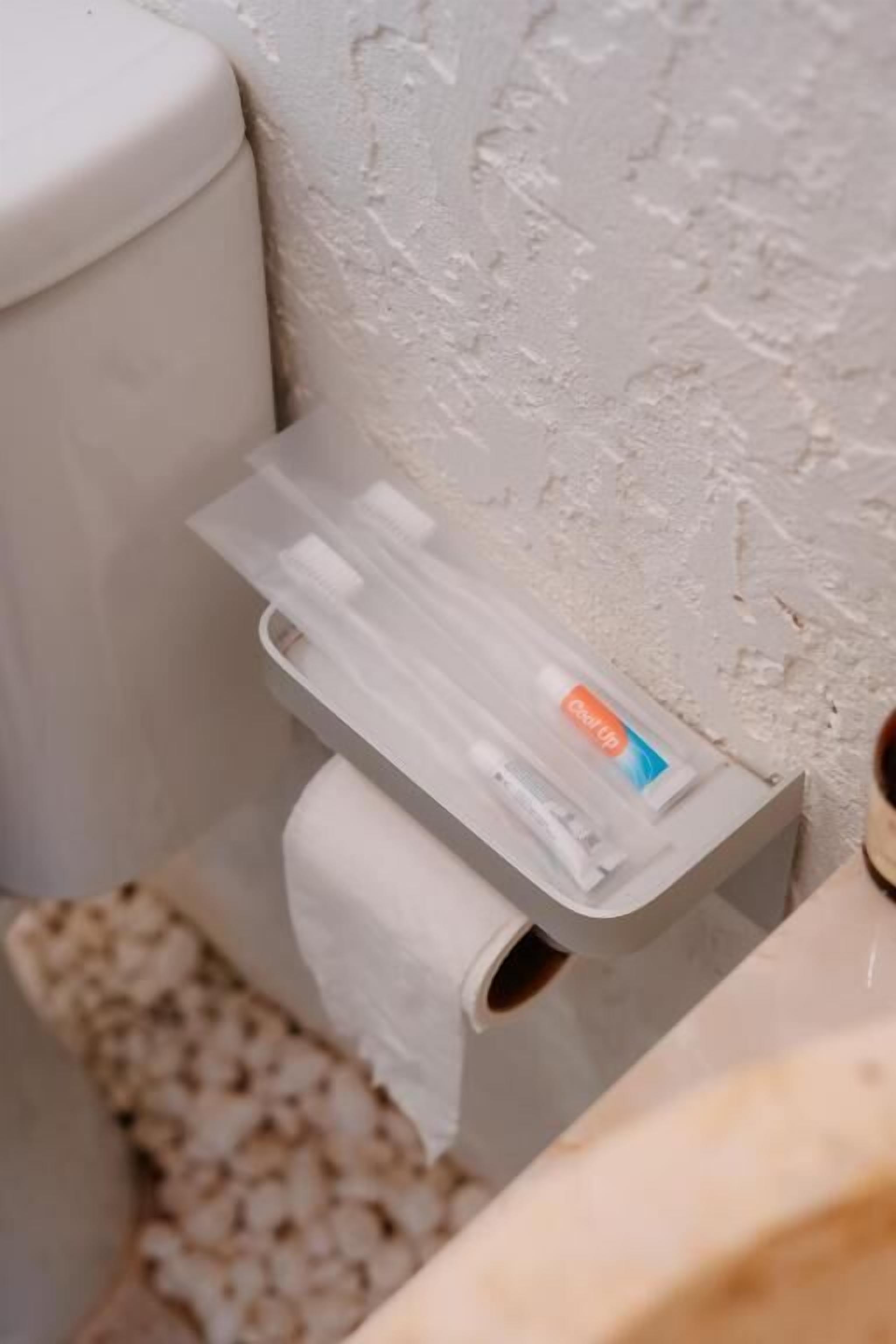 Un baño con un inodoro, un rollo de papel higiénico y una caja de pañuelos en un soporte.