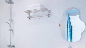 Un baño con inodoro blanco, lavamanos independiente con lavabo de piedra, ducha con cabezal de ducha de mano y espejo montado en la pared.