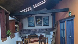 Un coin repas avec une table et des chaises en bois, une cuisine à l’arrière-plan et une porte bleue.