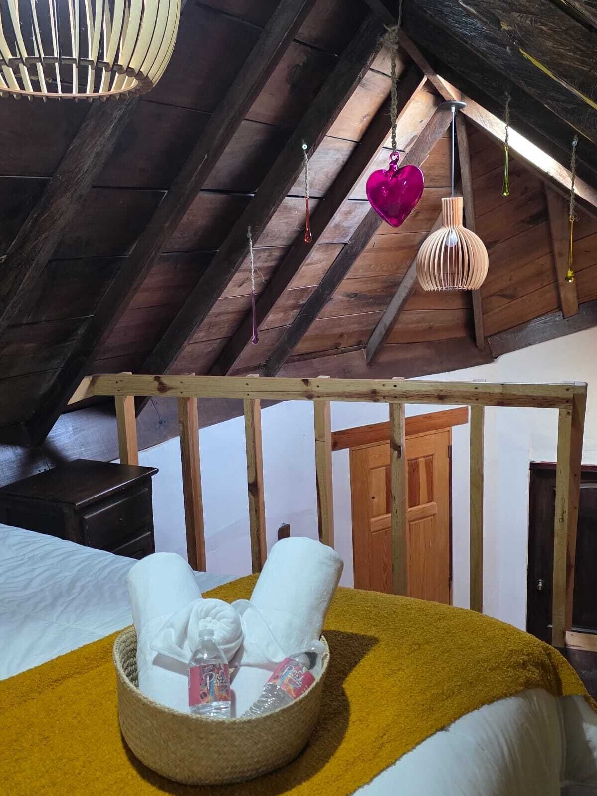 Un dormitorio acogedor en el ático con cama, mesita de noche, cabecero de madera y una lámpara colgante.
