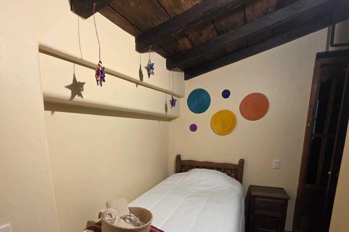 A bedroom with a wooden ceiling, a bed with a white duvet, a small bedside table, and a wall with colorful circular decorations.