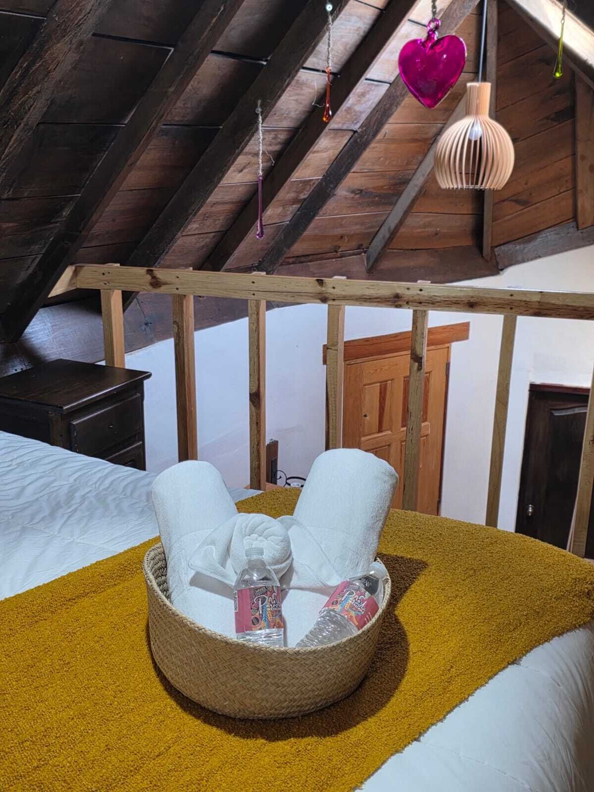 Una habitación acogedora con una cama, una mesita de madera y una silla de mimbre, además de toallas y artículos de aseo.