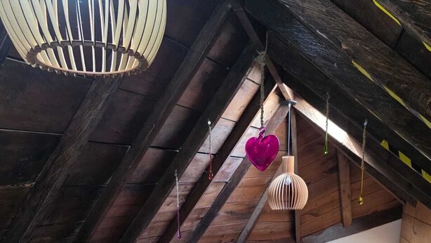Une pièce chaleureuse avec un lit, une tête de lit en bois, un luminaire suspendu et une porte visible au fond.