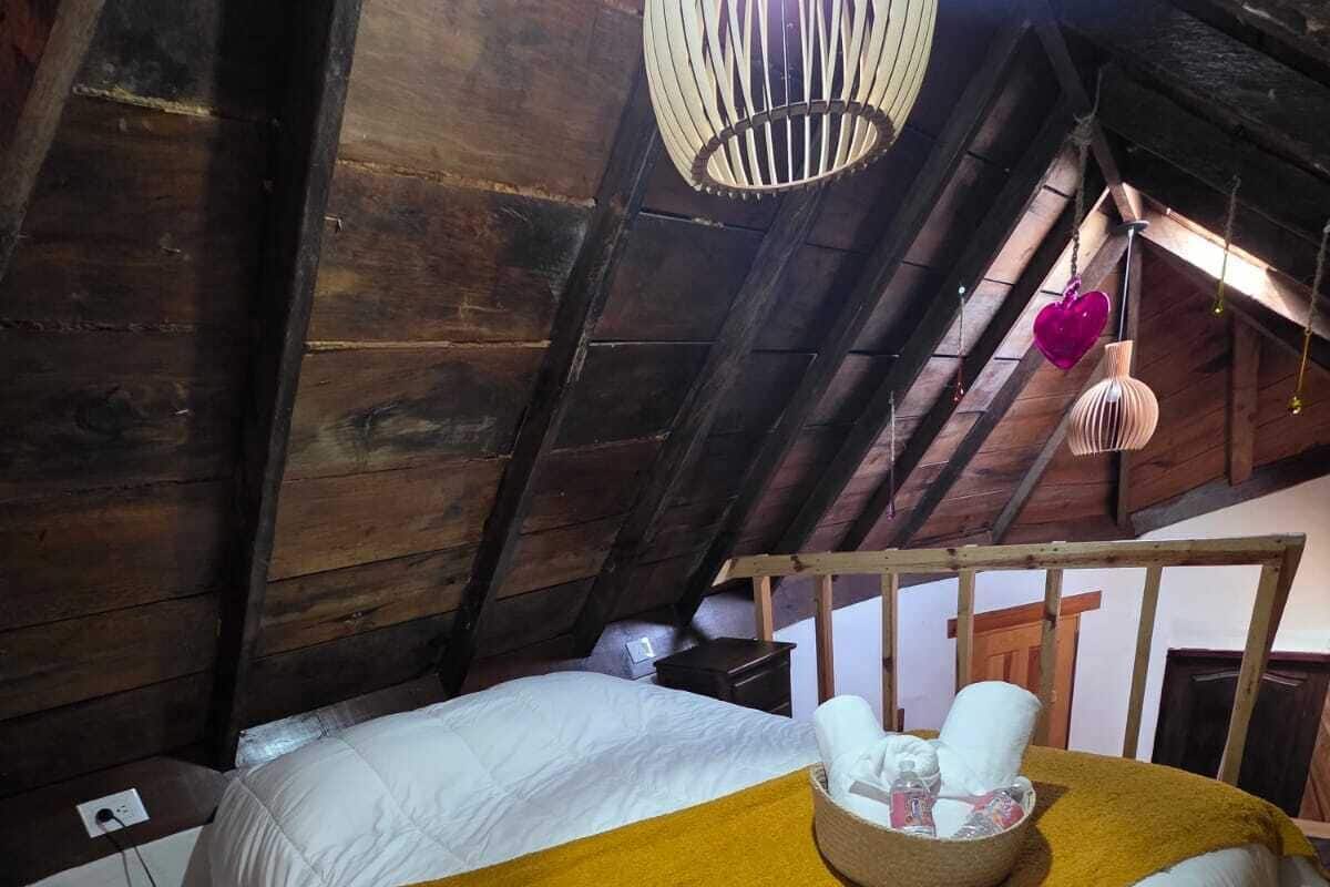 A cozy attic bedroom with a large bed, a wooden headboard, and a hanging light fixture.