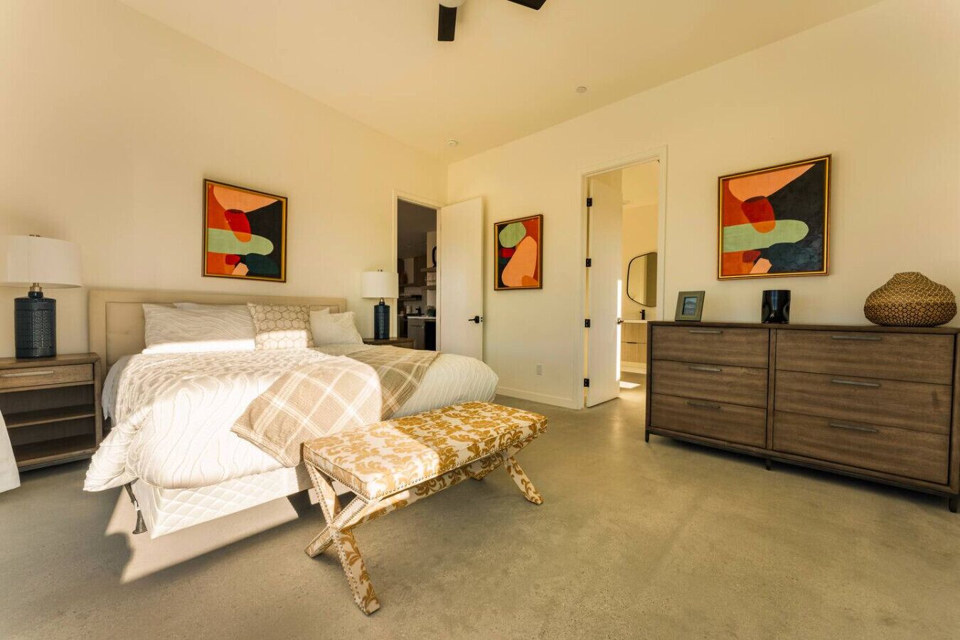 A bedroom with a bed, bench, dresser, and abstract art.