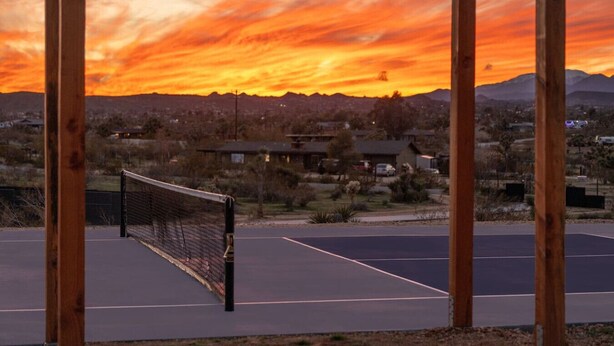 A tennis court with a wooden fence and a sunset view. - Inez Retreat | Pool | Spa | Pickleball Court (Yucca Valley)
