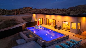 A modern building with a swimming pool, outdoor seating, and a desert landscape at night. - Inez Retreat | Pool | Spa | Pickleball Court (Yucca Valley)