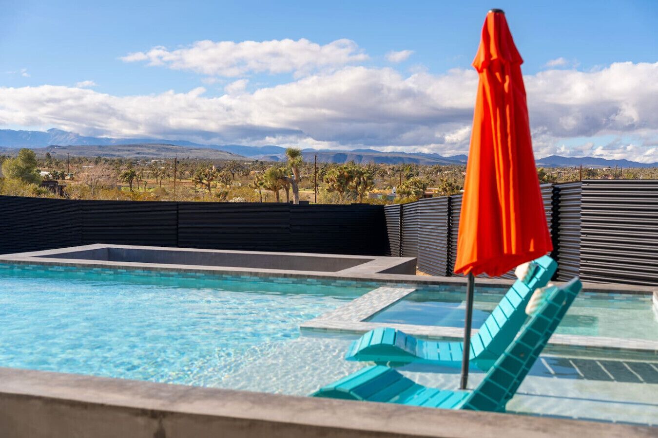 A swimming pool with clear blue water, a red umbrella, and a view of distant mountains.