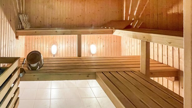A sauna room with wooden benches, a tiled floor, and two wall-mounted light fixtures.