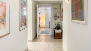 A hallway with a tiled floor, framed artwork on the walls, a lamp, and a small table with a plant.