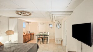 A bedroom with a bed, a desk, and a chair, a dining area with a table and chairs, and a TV mounted on the wall.