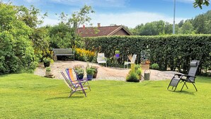 A garden with a bench, chairs, and a house in the background.