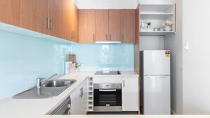 A compact kitchen with wooden cabinets, a built-in oven, a refrigerator, and a small countertop with a sink. - Loft Life Footscray Near Cafes & CBD (Footscray)